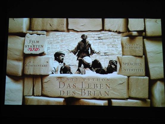 Abfotografiertes DVD-Menü. Eine sandfarbene Steinmauer, mittig ein großes Loch, durch das eine Filmszene zu sehen ist. Darunter in den Stein gemeißelt: „Monty Pyrhon - Das Leben des Brian“. Links und rechts verschiedene Menüpunkte, „Film starten“ oben links ist markiert.