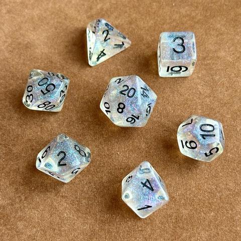 Picture of a set of transparent polyhedral dice with black numbers & blue-purple glitter inside, sitting on a brown felt background.