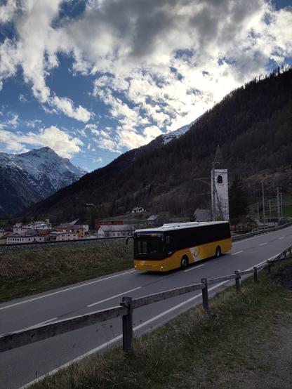 Foto. Berglandschaft mit Dorf und einem gelben Bus.