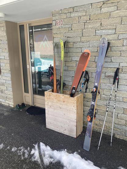 The doctor office entrance, with its own ski rack outside the door. It has 3 pairs of skis in it, and another pair leaning against the wall next to it.