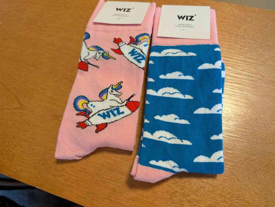 Two pair socks from Wiz in the Villages at Bsides. One are pink with a unicorn with blue and yellow mane & tail. The other are blue with white clouds, and the top band and toe are pink