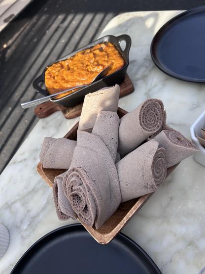 A black rectangular ceramic pot containing an orangey-gold shiro stew with a serving spoon in it