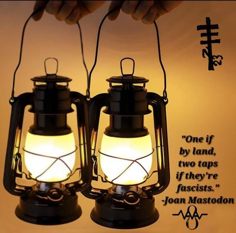Two antique lanterns are lit and being held. The quote says "one if by land, two taps if they're fascist." Joan mastodon resistance International