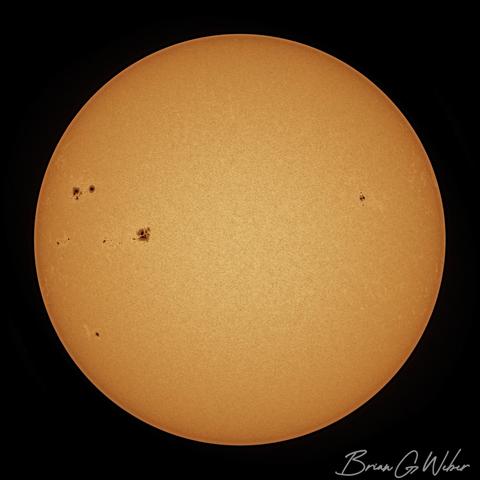 A full disk image of the sun with a few large clusters of sunspots on the left side