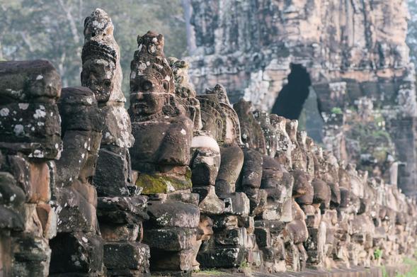Carved stone figures line a walkway with a tall stone wall behind it at the Angkor Thom South Gate, Siem Reap, Cambodia.