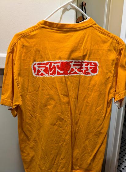 photo of a yellow T-shirt (back view) that has across the center in 3 inch tall Chinese in stylized white on orange background paint font. The Chinese characters are:
反你友我