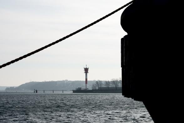 Part of a ship with a rope in the foreground, a lighthouse in the background