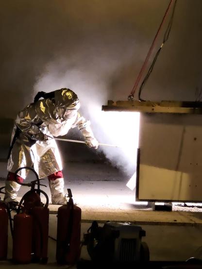 Person in a firesuit stocking a white hot fire.