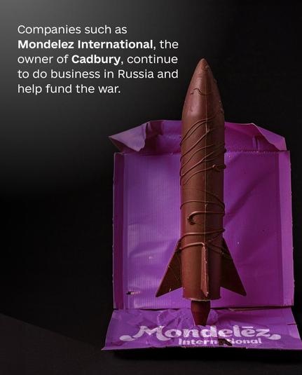 The image depicts a chocolate rocket wrapped in a purple Cadbury packaging, with the branding "Mondelez International" visible at the base. The accompanying text states: "Companies such as Mondelez International, the owner of Cadbury, continue to do business in Russia and help fund the war."

This image appears to be a critique of Mondelez International for its continued business operations in Russia, suggesting that these operations contribute to funding the ongoing conflict. The chocolate rocket symbolizes the company's products, while the text conveys a political message about the implications of their business decisions.