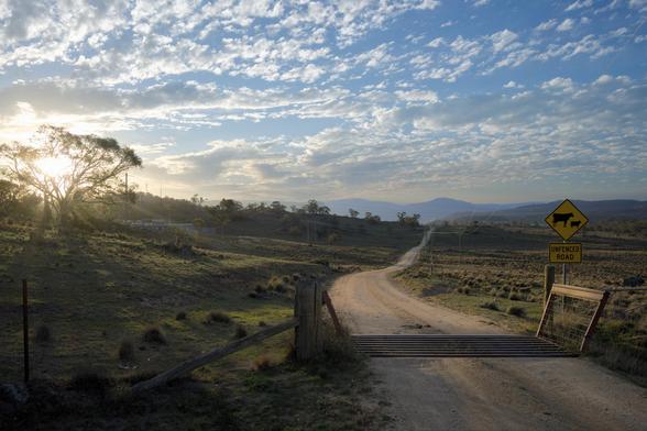 Landscape at sunset of a dirt road and a cattle grate with a yellow “unfenced road sign”
