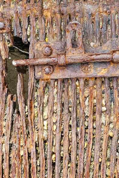 A rusty and corroded metal grill on the beach, with a bolt at the top.