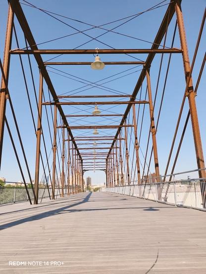 A pedestrian bridge in San Antonio Texas, Hays Bridge. It has a wooden floor, metal beams, metal fencing and lights on the middle beams.