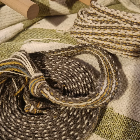 A coil of woven wool band in three colours, grey and white natural wool and plant dyed yellow