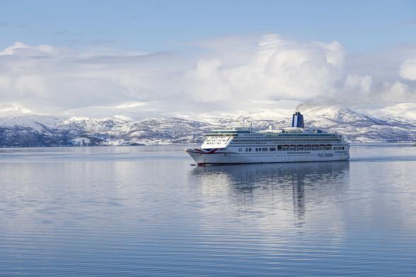 A bitterly cold but serene scene on almost mirror-like water in a wide fjord. Pale blue sky overhead becomes a bank of billowing white cloud over the distant landscape of undulating, deep snow-covered hills. Black patches of uncovered rock and the leafless trees on the landscape give it a bristled look. Between our position on this water and the land in the distance there is a cruise ship heading to our left and positioned as we look at the scene just off to the right. She's a small cruise ship as they go these days, mostly white-hulled except for a Union Flag painted on her sharp prow. A single dark blue funnel is towards the aft of the ship with some light smoke emerging and streaming backwards. It's just possible to make out figures on the top deck and the exposed parts of the promenade deck admiring this icy landscape and possibly our own ship as we pass one another.