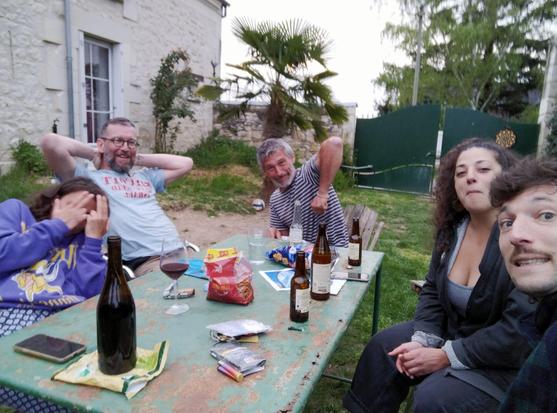 Tablée appéritif devant une maison paysanne avec des femmes et hommes souriants et déconnant ; un petit palmier derrière eux.