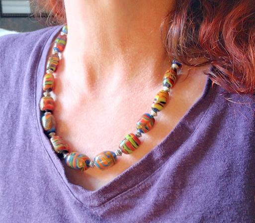 Image of a woman with red hair and a purple shirt wearing a multicolored handmade glass bead necklace