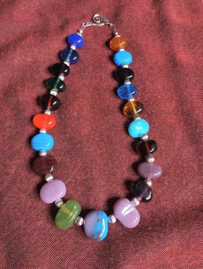 Image of a multicolored handmade glass bead necklace set against a dark red cloth background.