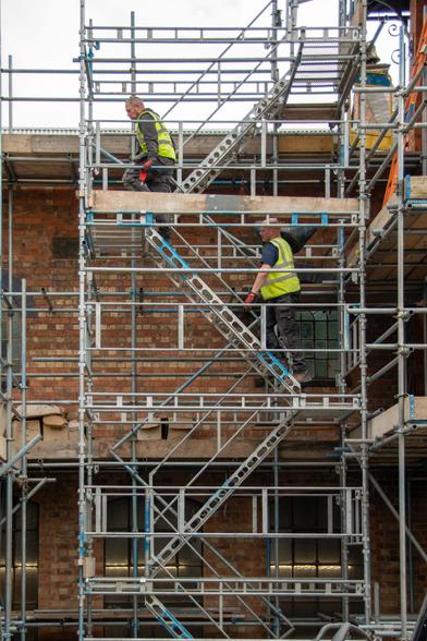 Scaffolding in front of a building; two men in hi-vis jackets climbing up.