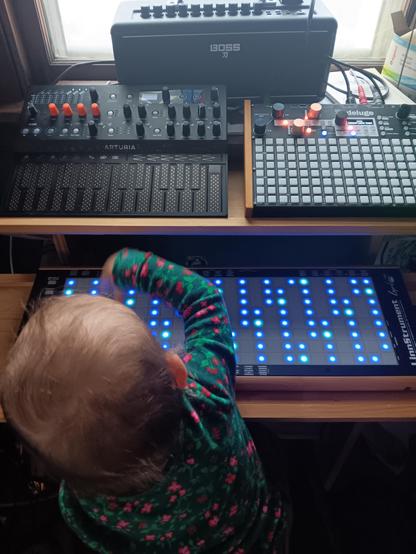A young child sits facing an array of electronic instruments with glowing lights on them