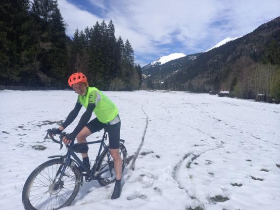 Un cycliste en tenue fluo et en short dans une prairie enneigée
