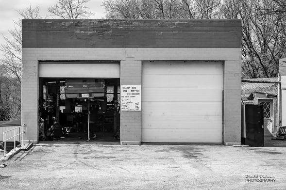 A small, two bay auto repair shop.  One door is open and you can see a pickup truck up on a lift.