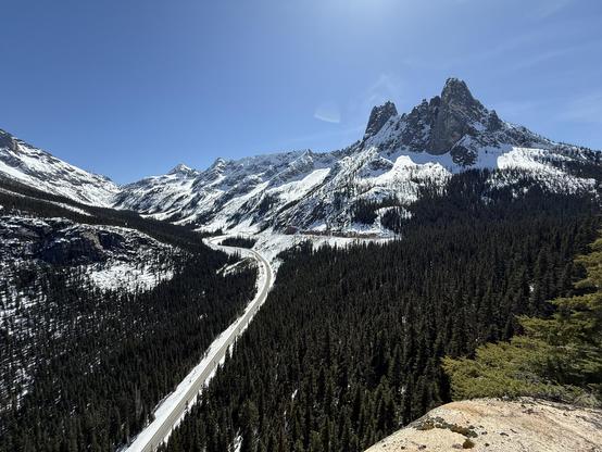 View from Washington Pass lookout of a mountain landscape, from Kangaroo Pass to the Early Winter Spires. The North Cascades Highway is visible below tracing a large hairpin turn.