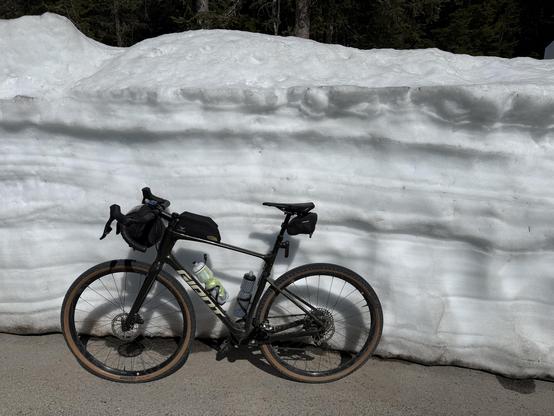 A bicycle leaning against a snowbank. The pavement is dry, the snowbank over 6 feet (2 meters) tall.
