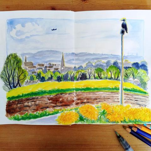 A double-page sketchbook with a watercolor of an agricultural landscape, with church steeples and houses in the distance. A crow perches on a lantern.

Doppelseite im Skizzenbuch mit Aquarell einer Agrarlandschaft, in der Ferne Kirchtürme und Häuser. Auf einer Laterne sitzt eine Krähe.