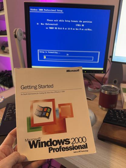 The Windows 2000 “getting started” guide book held up in front of the Windows 2000 drive formatting screen.