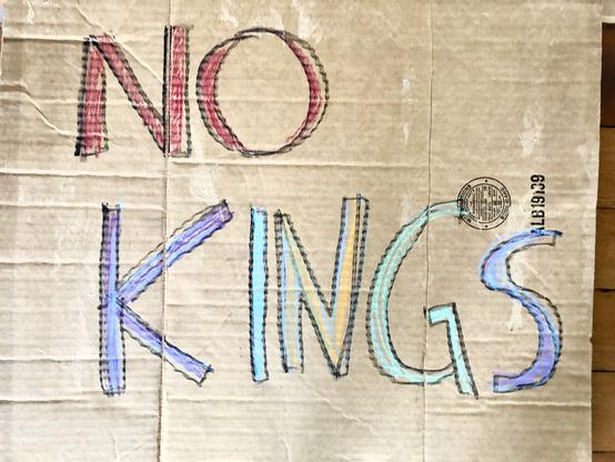 Cardboard sign hand scrawled with colorful words reading No Kings