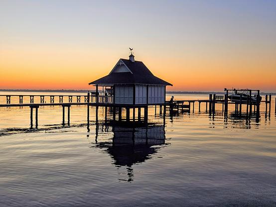 Pre-dawn view across an inlet of the Saint Johns River.  Private piers and boat docks appear as silhouettes against bands of warm colors rising at the horizon as sunrise approaches.
