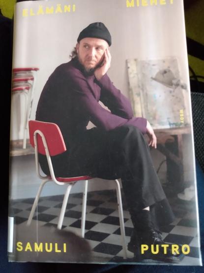 Kirjan kansi, jossa Samuli Putro istuu punaisella tuolilla ja nojaa päätään käteensä.