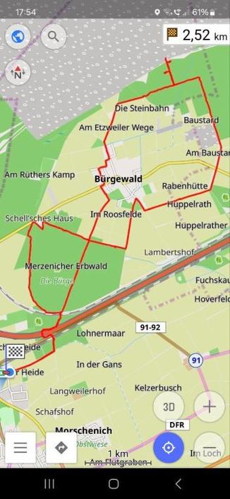 The image shows a digital map. It is part of a navigation interface as seen on a smartphone. In the centre of the map is the village of Bürgewald, surrounded by forest, fields and various landmarks. A red path marks a route.