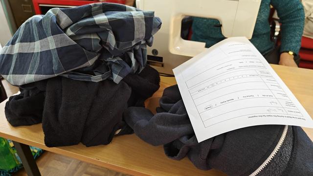 Clothes make up almost 24% of the items that we fix. This shows a pile of clothes that came to us today. There is a blue checked shirt, a fleece and another top. The repair form is on top of the pile of clothes.