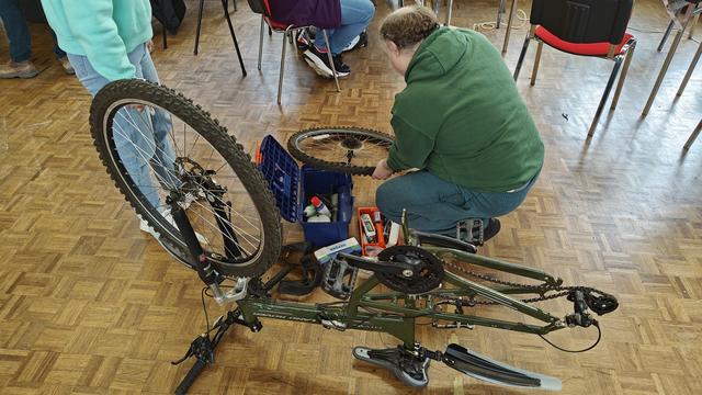 A man is fixing a mountain bike. The bike is upside down and the rear wheel has been removed.