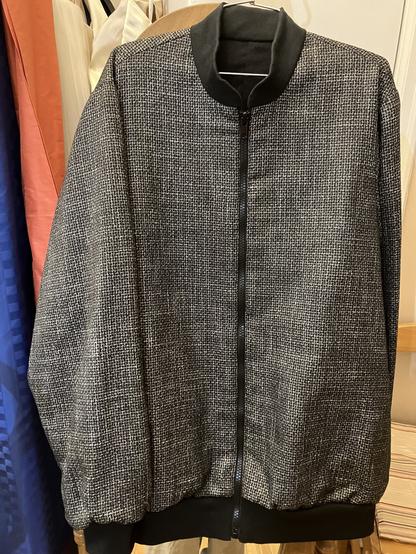 A black and white weave soft wool fabric bomber style jacket with black cuff, hip band and collar and exposed black zipper in centre front