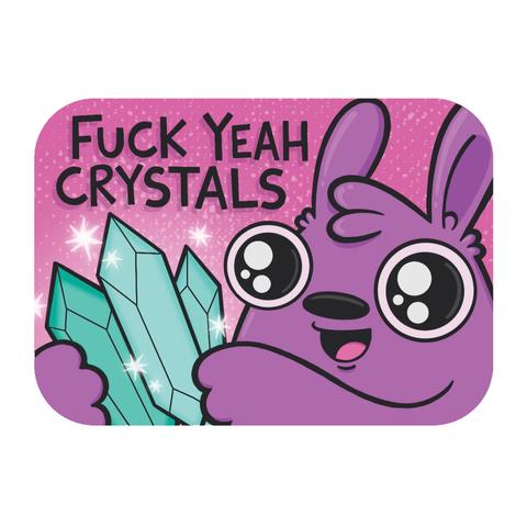 Illustration of a purple rabbit character on a pink background. Their eyes are wide and a smile is on their face. They are holding three sparkling blue crystals. The words “Fuck yeah crystals” appear at the top of the drawing.