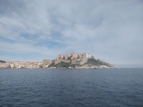 Photo de la citadelle de Calvi prise depuis la mer. Le ciel est un peu nuageux.