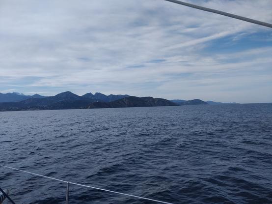 Photo de la mer avec au fond la Corse, on peut voir des sommets enneigés. Le ciel est un peu nuageux.