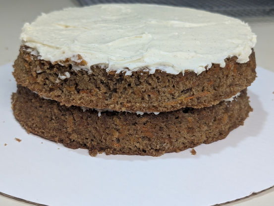 Photo of a stack of two cakes, carrot cake with the orange flecks visible. There's a lot of frosting between the two, and on top, speckly, but none on the sides.