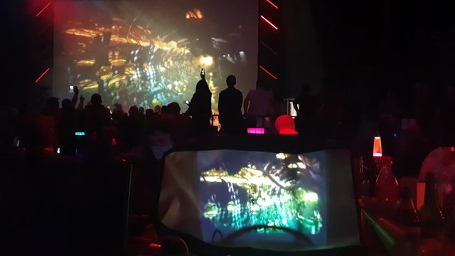 A projector showing "the scene is dead" on a bike bag. In the background a huge projection of the same demo and a lot of people dancing.