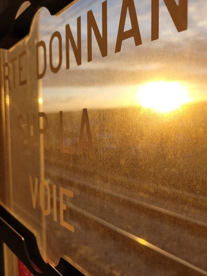 Lever de soleil derrière une vitre du train où on devine l'inscription "porte donnant sur la voie"