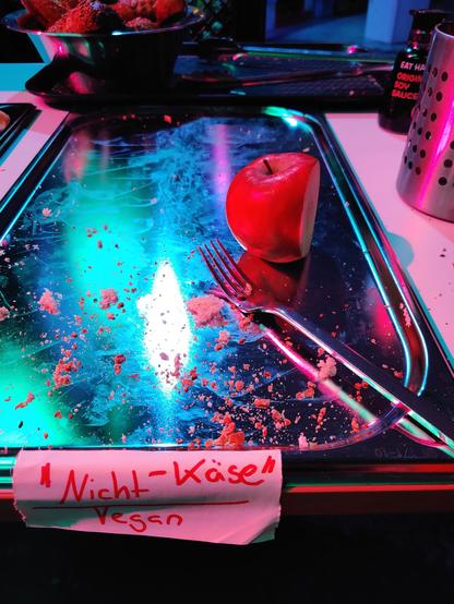 A stainless steel platter with a single fork and part of an apple. The Platter is labeled as "Nicht-Käse", vegan