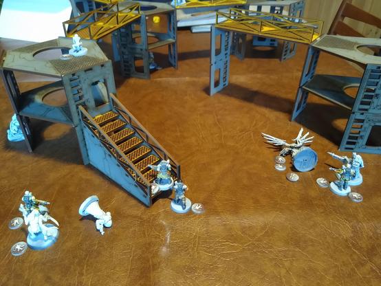 A wargaming board with a game of Necromunda underway. A couple models from each opponent are pinned or seriously injured. The others scramble to desecrate the opposing icon and take out the opposing gang members.