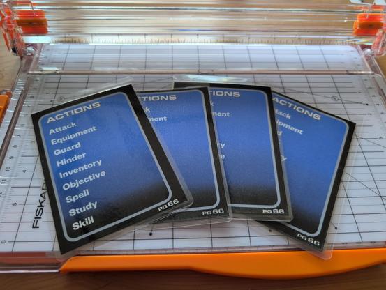 A set of four laminated cards sitting on a paper cutter. Each card has FF7-style menus listing available actions for combat in Fabula Ultima.