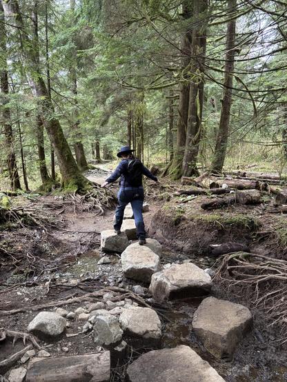 A woman walking along large rocks hopping from each one.