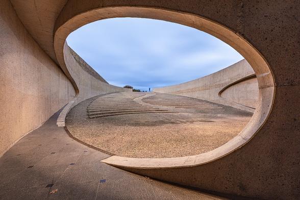 Look through the opening of a passageway underneath a motorway bridge in Vroenhoven in Belgium at dusk. Stairs and a pathway are leading up the view towards the silhouette of a man leaving the area. The silhouette is slightly blurry and ghostly as a result of a slow exposure.
