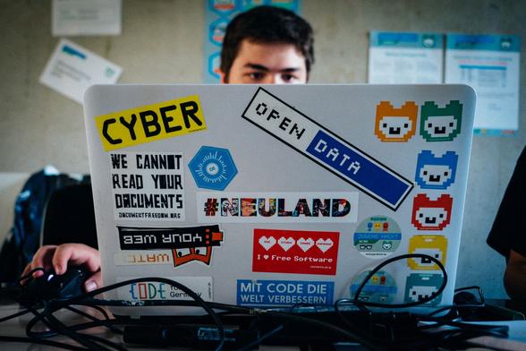 Blick auf den mit vielen bunten Stickern beklebten Laptop eines Jugend-hackt-Teilnehmis beim Hackathon. Neben bunten Alpaka-Köpfen, die für jede Teilnahme stehen, gibt es Sticker mit „OpenData“, „Mit Code die Welt verbessern“, #Neuland, „I love free Software“, „we cannot read your documents“ von documentfreedom.org, „Code for Germany“, „watch your web“ und natürlich „ CYBER“