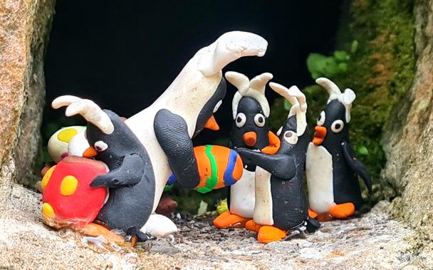 A small model penguin dressed as the Easter Bunny handinh out Easter eggs to smaller penguins with bunny ears on.