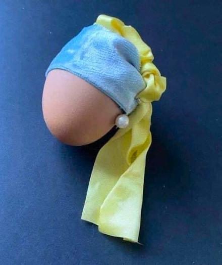 Een ei opgetuigd als Het Meisje Met De Parel simpel door een blauw fluwelen lint om het ei te wikkelen met een geel doek en onder het lint, ter hoogte van een oor, een pareltje.